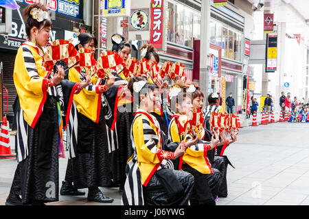 Japan, Kumamoto, Hinokuni Yosakoi dance festival. Teenage women team, wearing black and yellow yukata, kneeling and holding fans, in shopping mall.