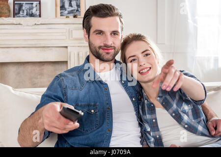 Young couple sitting on sofa and using tv remote control Stock Photo