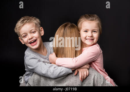 Mother carrying two adorable happy kids on black