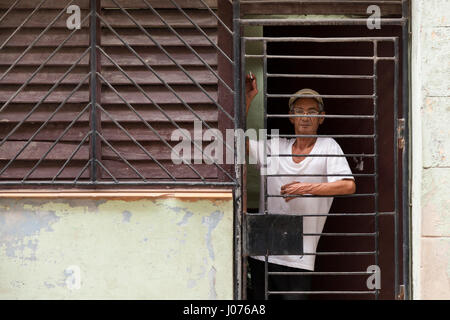 A Cuban man looking outside his home through security bars in Old Havana, Cuba. Stock Photo