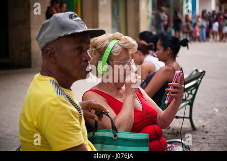A Cuban woman looks at her smartphone while using Beats by Dre headphones in Old Havana, Cuba. Stock Photo