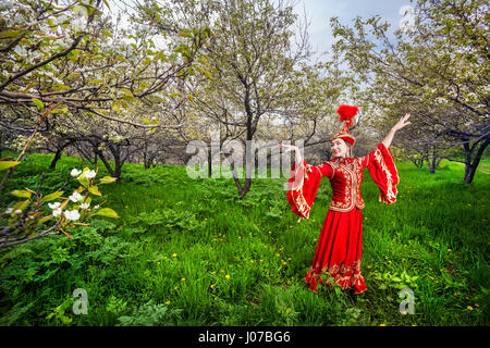 Kazakh woman dancing in red dress at Spring Blooming garden in Almaty, Kazakhstan Stock Photo