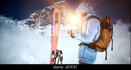 Skier with skis and backpack using mobile phone against view of snowy mountain range and clouds Stock Photo