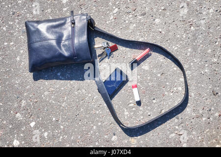 Handbag, cellular phone with broken screen, keys and lipstick on asphalt street, conceptual picture. Stock Photo