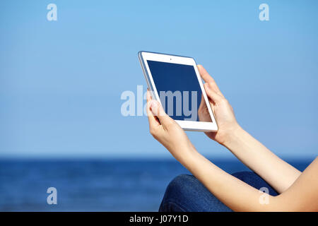 Close up picture of female hands with tablet computer on a beach, blank screen with copy space. Stock Photo