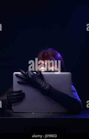 Hacker in mask holds laptop Stock Photo