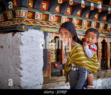 A woman carrying a baby spins prayer wheels on the wall of the Changangkha Lhakhang Temple in Thimphu Bhutan Stock Photo