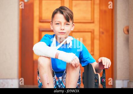 Mischievous boy with broken hand injured after accident on skateboard. Stock Photo