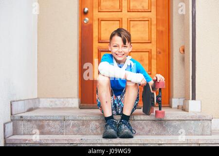 Mischievous boy with broken hand injured after accident on skateboard. Stock Photo