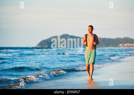 Young man with backpack walking on the beautiful beach. Stock Photo