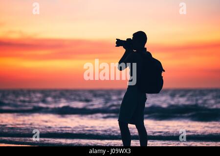 Silhouette of the young photographer. Photo shooting during amazing sunset on the tropical beach. Stock Photo