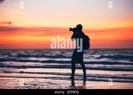 Silhouette of the young photographer. Photo shooting during amazing sunset on the tropical beach. Stock Photo