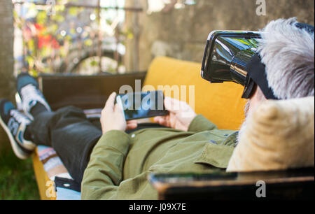 Senior man using virtual reality on a sofa bed outdoors Stock Photo