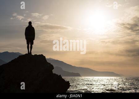 Hiker or runner silhouette backpacker, man looking at inspirational ocean landscape and islands on mountain peak. Accomplished man celebrate beautiful Stock Photo