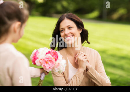 girl giving with flowers to mother in summer park Stock Photo