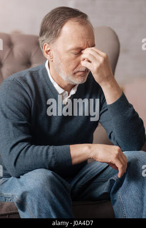Blind headache. Close up of senior man having terrible headache and touching nasal bridge with fingers. Stock Photo