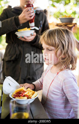 Child eating a bowl chips with ketchup in a pub garden Stock Photo