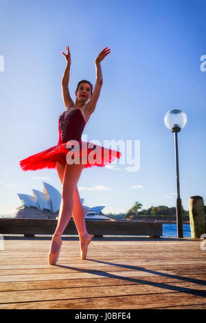 Young fit ballerina in point shoes and concert tutu stretching in a ballet setting on a street in warm sunrays against blue sky. Stock Photo