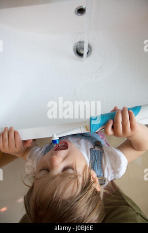 Girl toddler brushing her teeth using an adult electric toothbrush. She is 16 months old