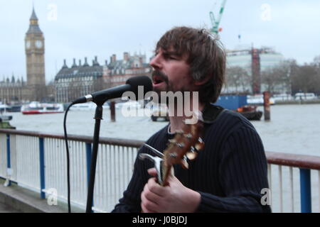 street musician busker on south bank of river thames with parliament in background from london Stock Photo
