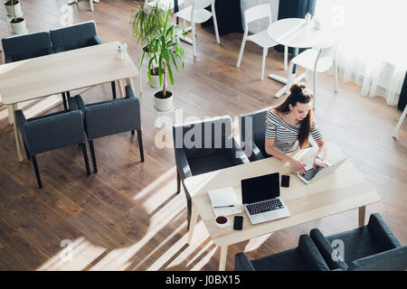 Overhead view of businesswoman at table of staff canteen, typing on a laptop. Stock Photo