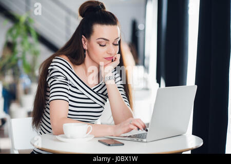 Bored woman surfing the internet in a cafe with a cup of coffee. Stock Photo