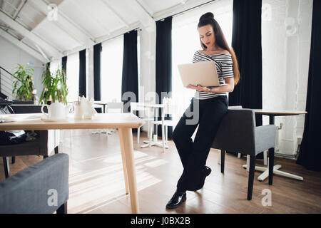 Young attractive brunette woman holding a laptop and typing, while looking at the screen. Stock Photo