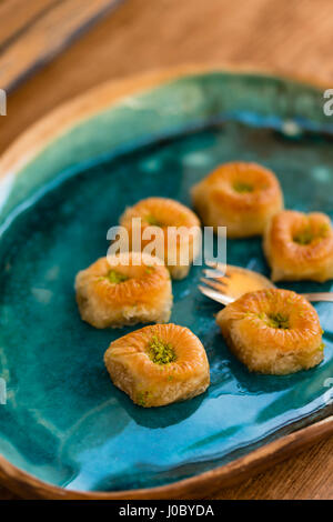 Six baklava with pistachio placed in turquoise ceramic tray with golden fork placed on wooden tabletop Stock Photo