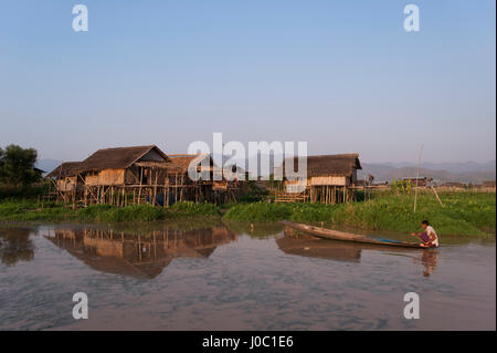 A man paddles his canoe past one of the floating villages on Inle Lake, Myanmar (Burma), Asia Stock Photo