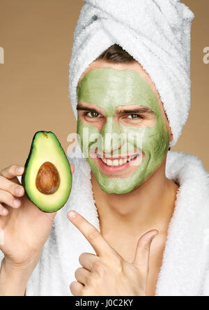 Happy smiling man with facial mask of avocado. Photo of well groomed man receiving spa treatments. Grooming himself Stock Photo