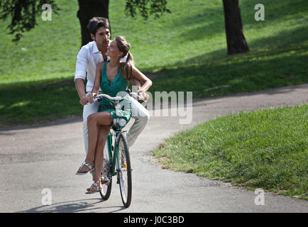 Young couple riding bicycle through park, Turin, Piedmont, Italy Stock Photo