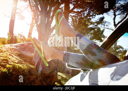 Young woman lying in car, legs dangling out of car window Stock Photo