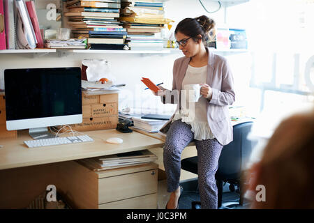 Woman sitting on desk looking at notepad Stock Photo