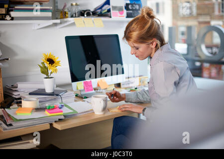 Woman sitting at desk in office writing on notepad Stock Photo