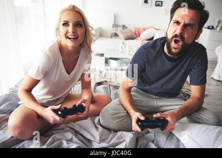 Couple sitting on bed, holding computer controllers, playing computer game Stock Photo