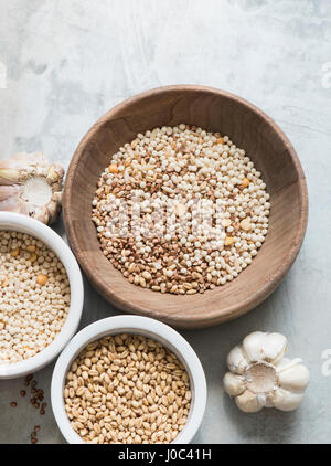 Different types of grains in bowls, garlic bulbs beside bowls, overhead view Stock Photo