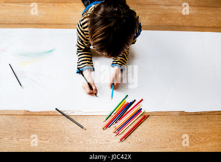 Overhead view of boy lying on floor drawing on long paper