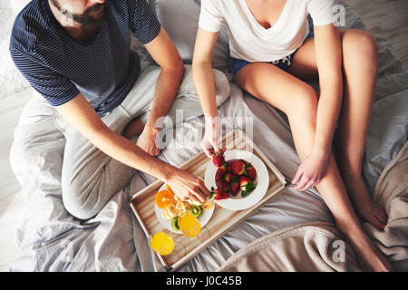 Couple relaxing on bed, eating strawberries, elevated view Stock Photo