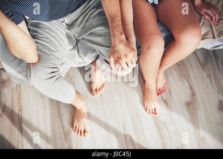 Couple sitting on edge of bed, holding hands, overhead view Stock Photo