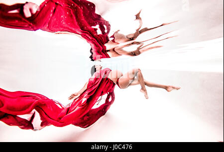 Underwater view of poised young pregnant woman with flowing red textile Stock Photo