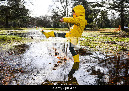 Boy in yellow anorak splashing in park puddle Stock Photo