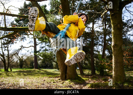 Boy in yellow anorak swinging from park tree Stock Photo