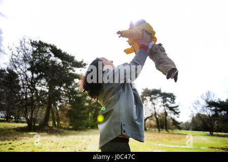 Mature woman holding up and playing with baby son in park
