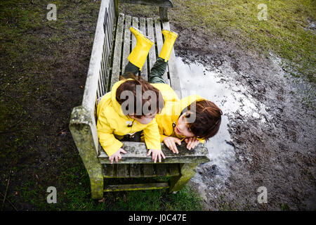 Overhead view of baby boy and brother in yellow anoraks on park bench Stock Photo