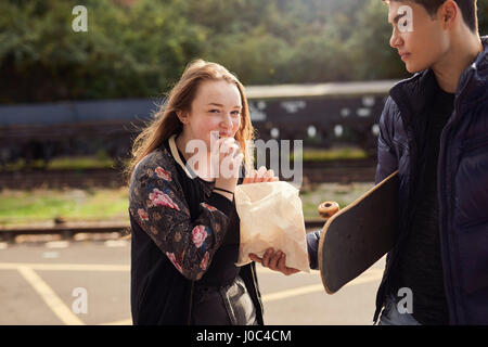 Young man sharing bag of chips with young woman,  skateboard under young man's arm, Bristol, UK