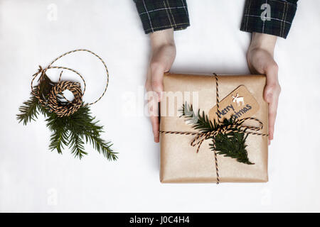Woman holding Christmas gift wrapped in brown paper, decorated with fern and string, overhead view Stock Photo