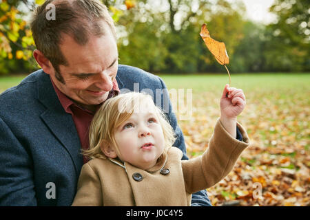 Daughter sitting on father's lap holding autumn leaf Stock Photo