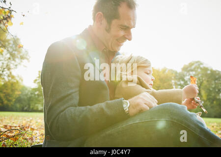 Daughter sitting on father's lap holding autumn leaf Stock Photo