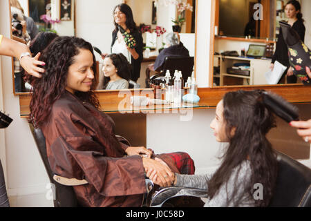 Girl and mother holding hands while having their hair styled in hair salon Stock Photo