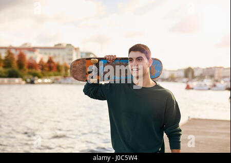 Young man walking beside river, carrying skateboard, Bristol, UK Stock Photo